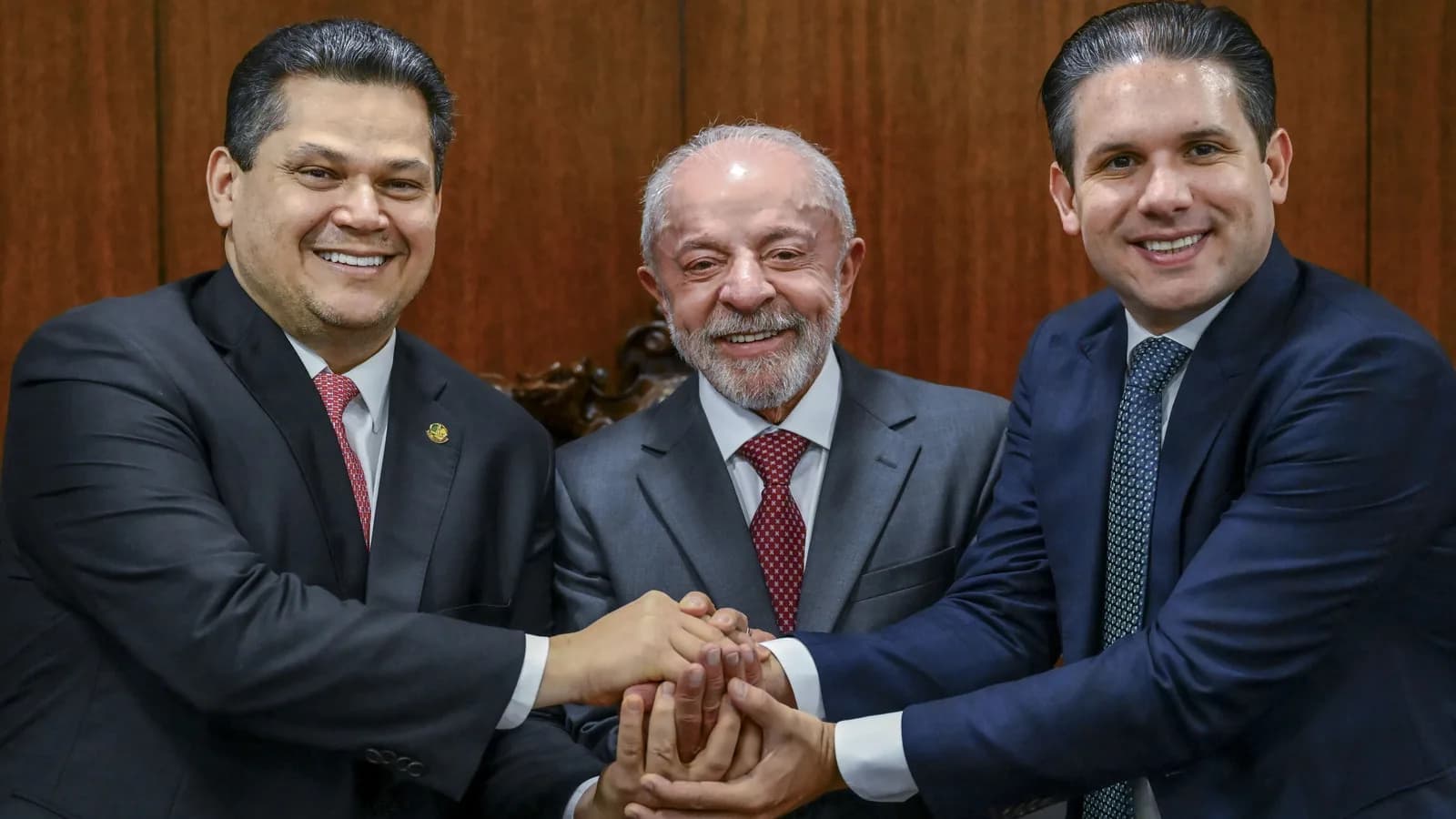 Lula sorri ao cumprimentar dois parlamentares em sessão solene de promulgação de emendas constitucionais na Câmara