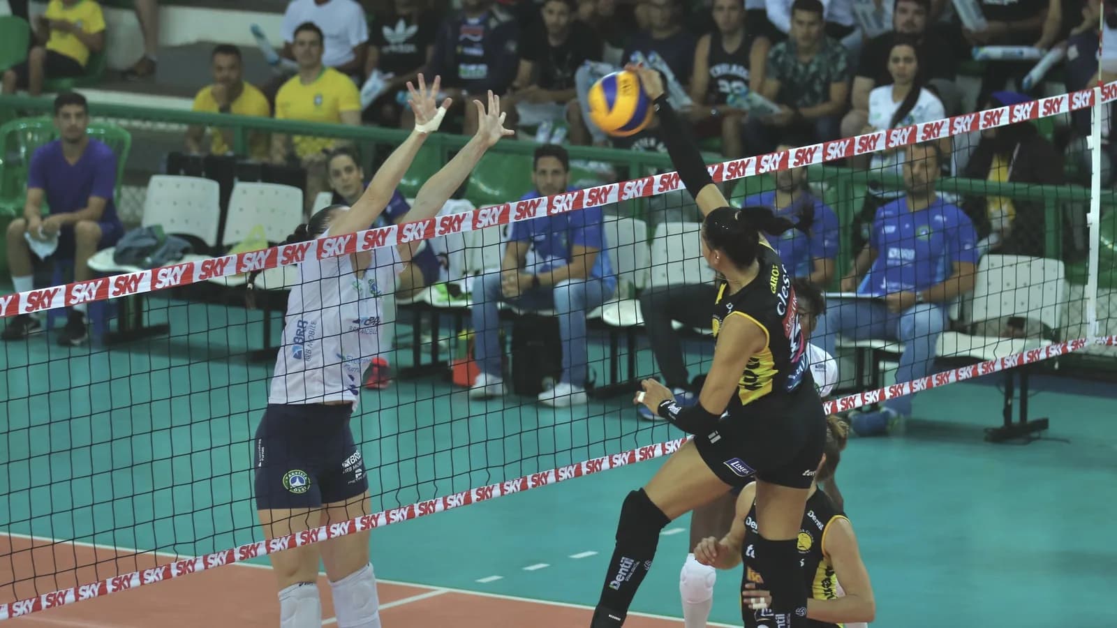 Jogadoras disputam bola perto da rede em partida de vôlei entre Brasília Vôlei e Praia Clube