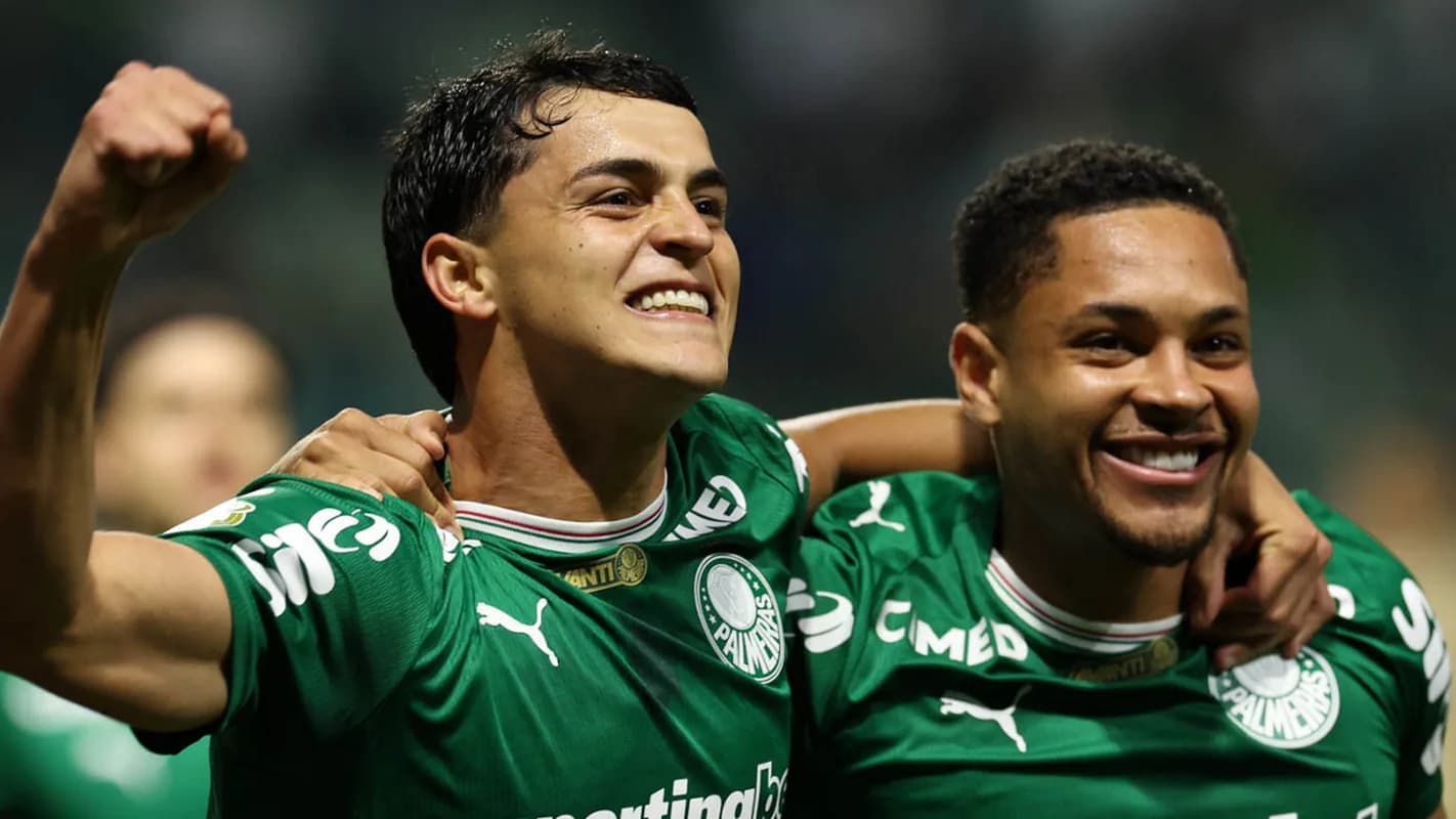 Dois jogadores do Palmeiras comemoram gol abraçados, com uniforme verde
