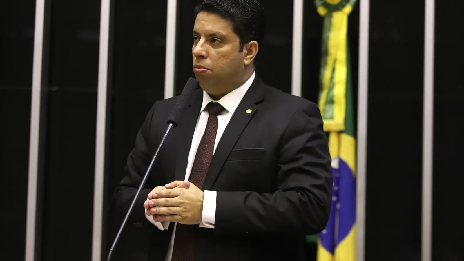 Deputado discursa à tribuna no plenário da Câmara dos Deputados, com bandeira do Brasil ao fundo