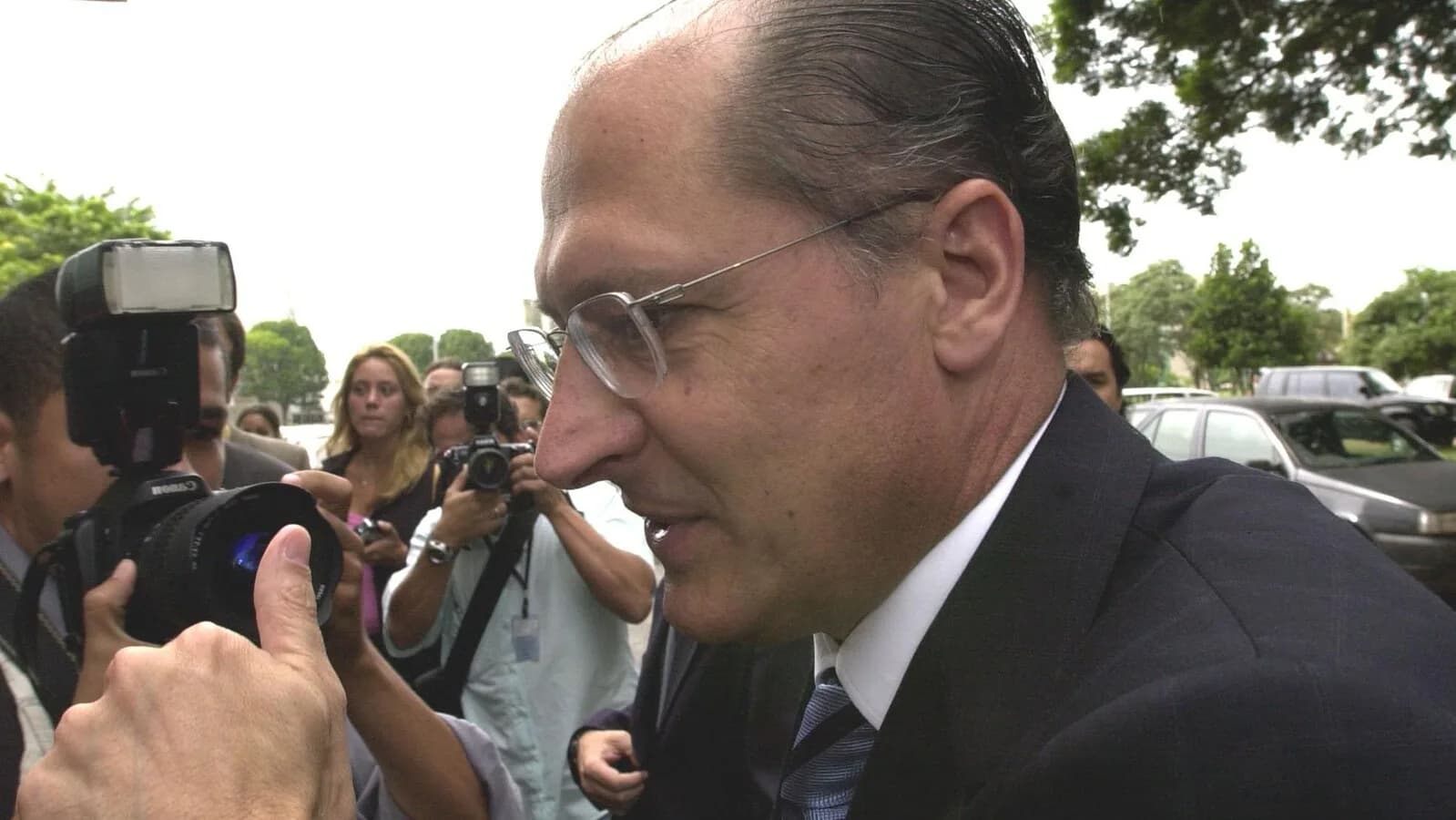 Geraldo Alckmin, de óculos e terno escuro, cercado de fotógrafos durante entrevista