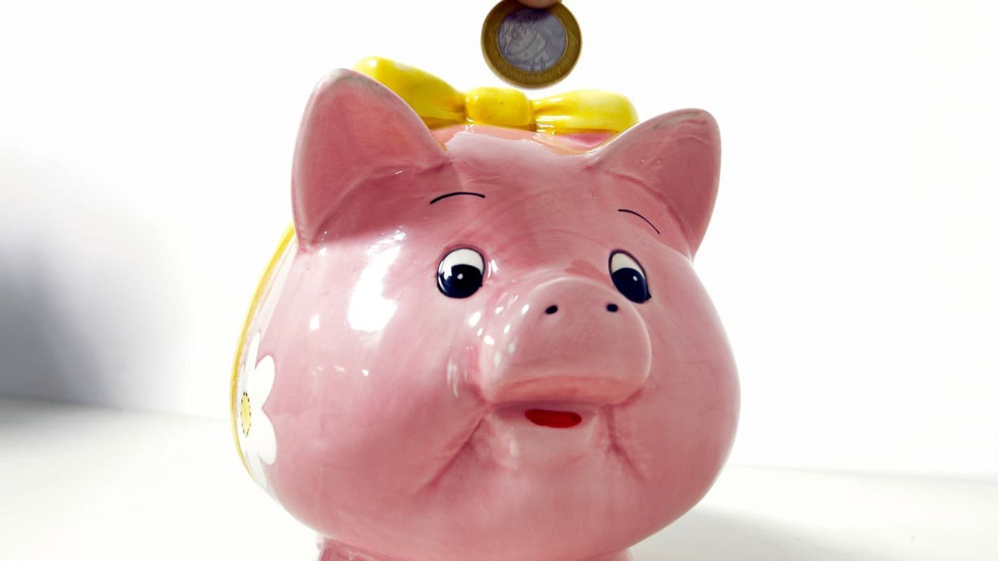 Moeda de um real sendo depositada em um cofrinho em formato de porquinho