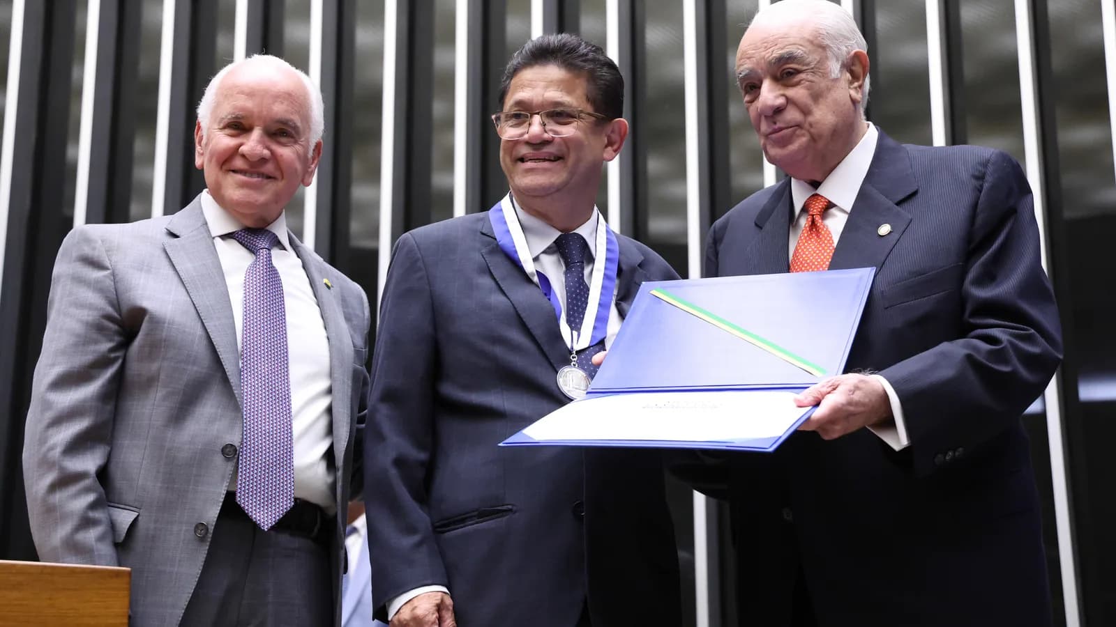 O vereador Isac Félix dos Santos recebe medalha ao lado de outras duas autoridades em cerimônia na Câmara dos Deputados
