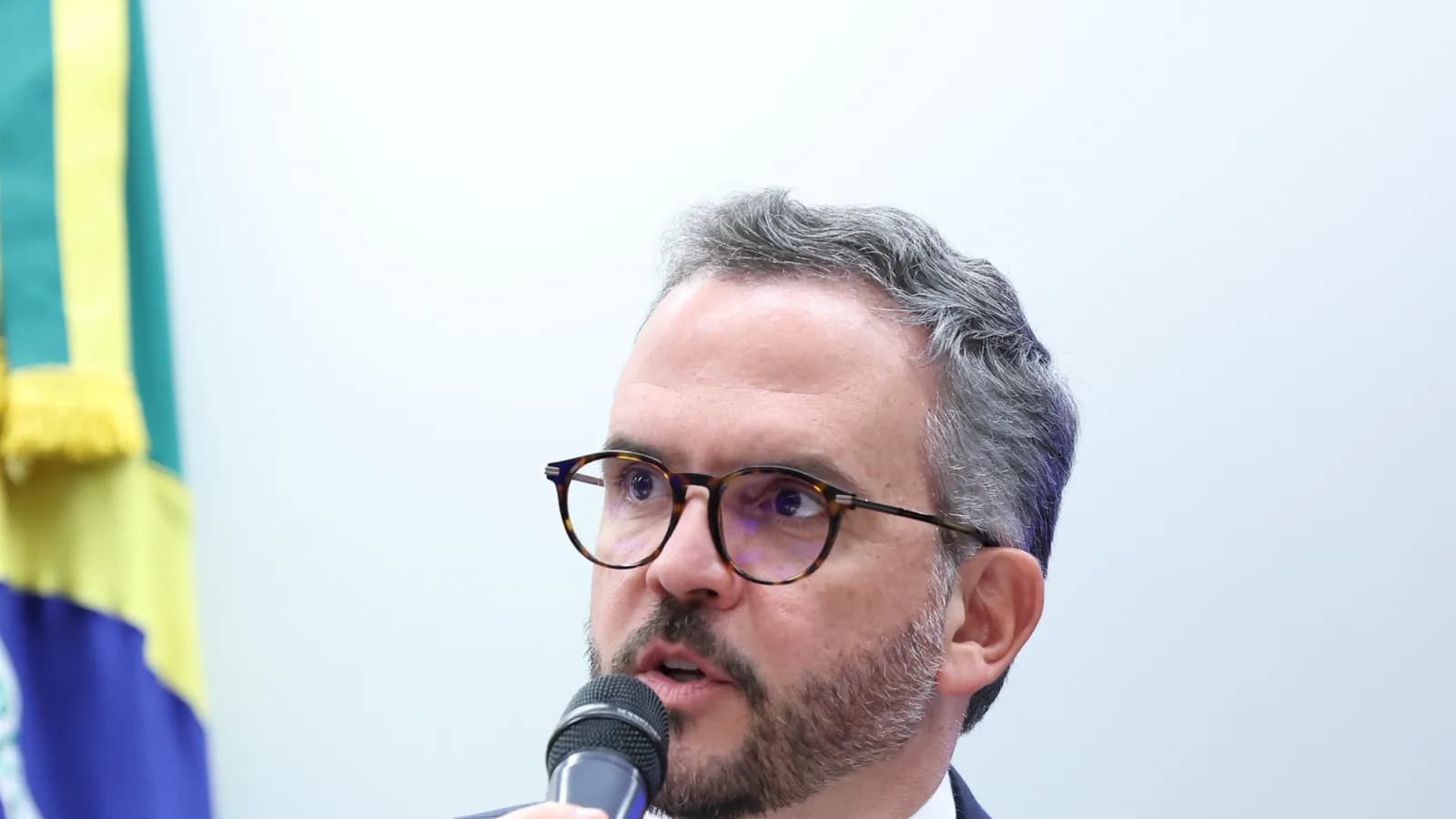 O ministro de Portos e Aeroportos, Tomé França, de óculos e terno azul-marinho, fala ao microfone durante audiência pública
