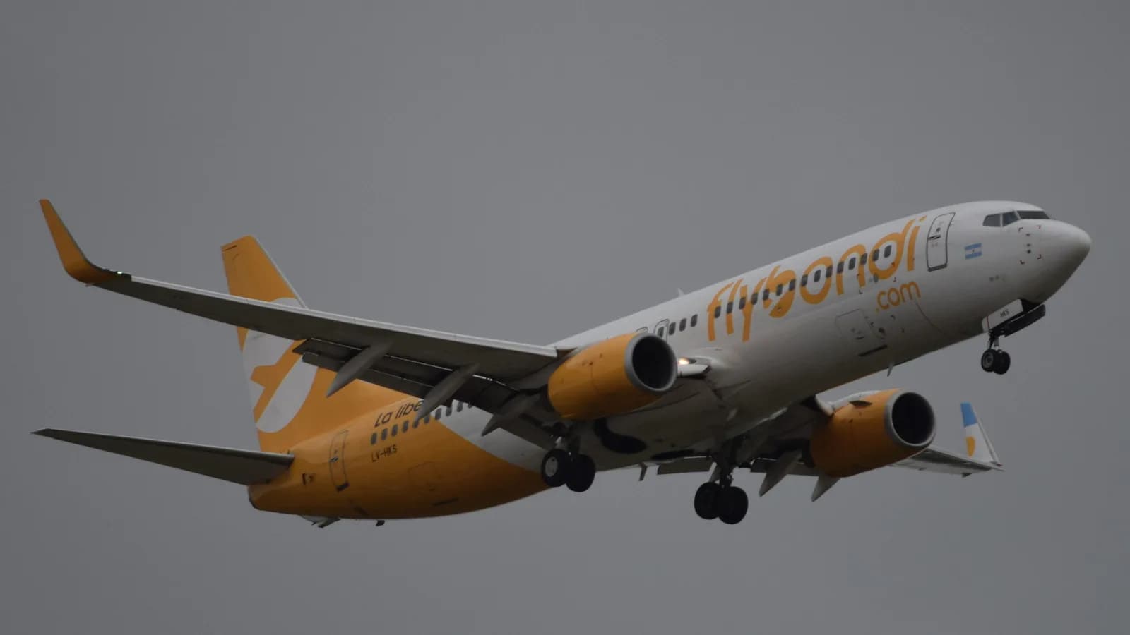 Avião da companhia aérea Flybondi em voo, com a pintura amarela e o nome da empresa na fuselagem