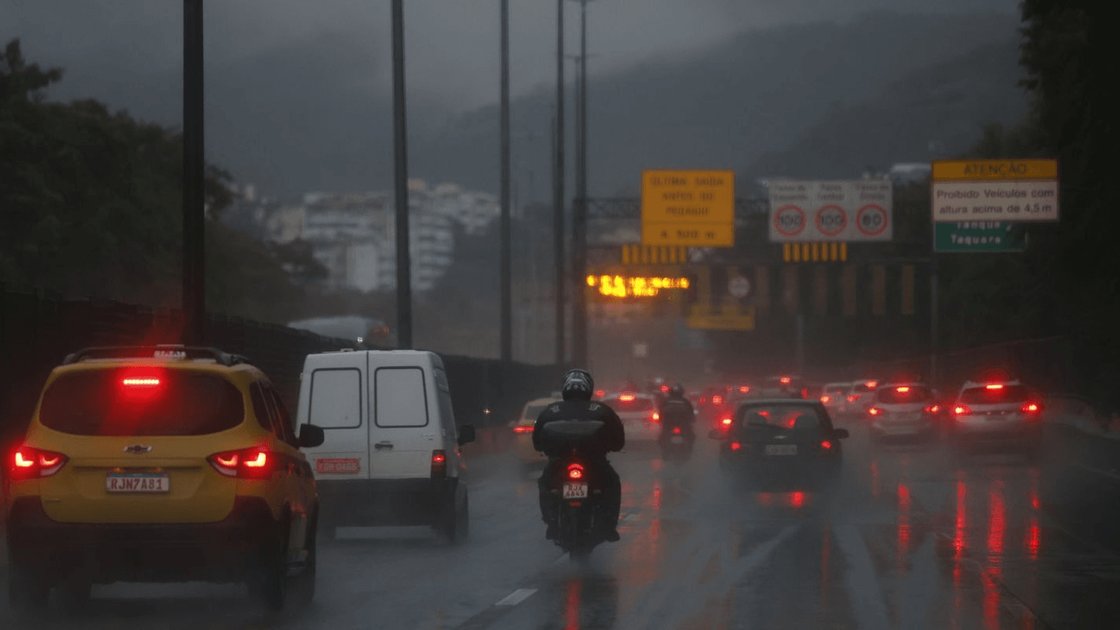Carros e motociclista trafegam sob chuva forte em via expressa no Rio de Janeiro
