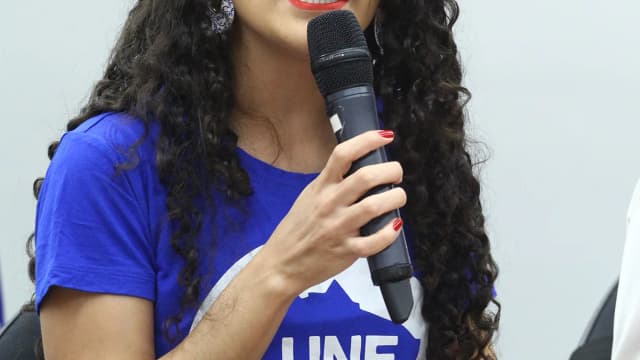 Diretora da UNE, vestindo camiseta da entidade, discursa ao microfone em audiência pública na Câmara