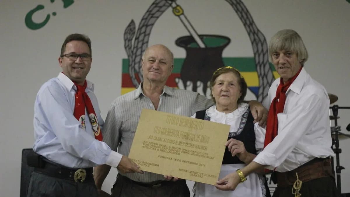 Grupo de pessoas em trajes tradicionais gaúchos participa de cerimônia em evento de CTG