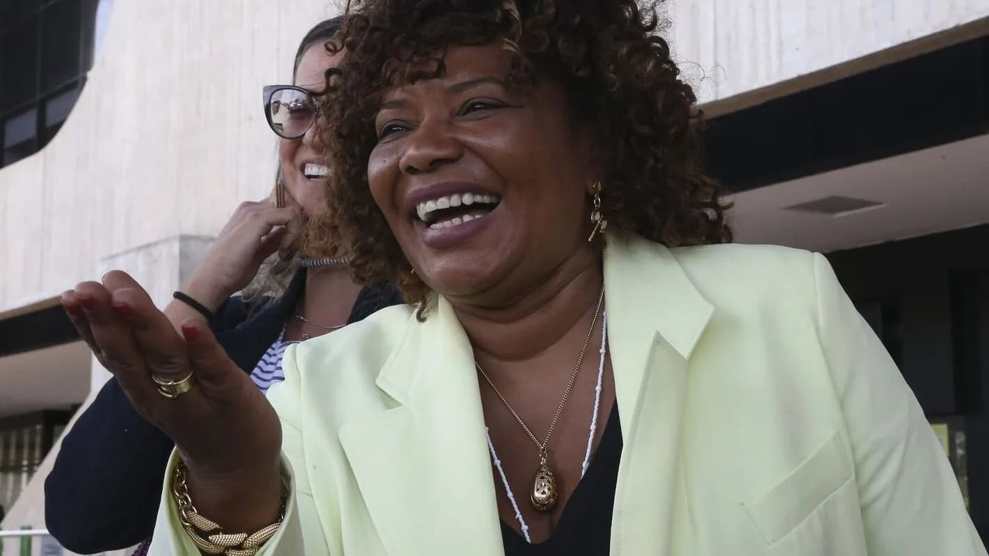 Ministra Margareth Menezes sorri em frente a prédio de arquitetura modernista em Brasília