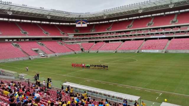 Times perfilados em campo antes de partida na Arena de Pernambuco, estádio do Santa Cruz, com arquibancadas vermelhas ao fundo