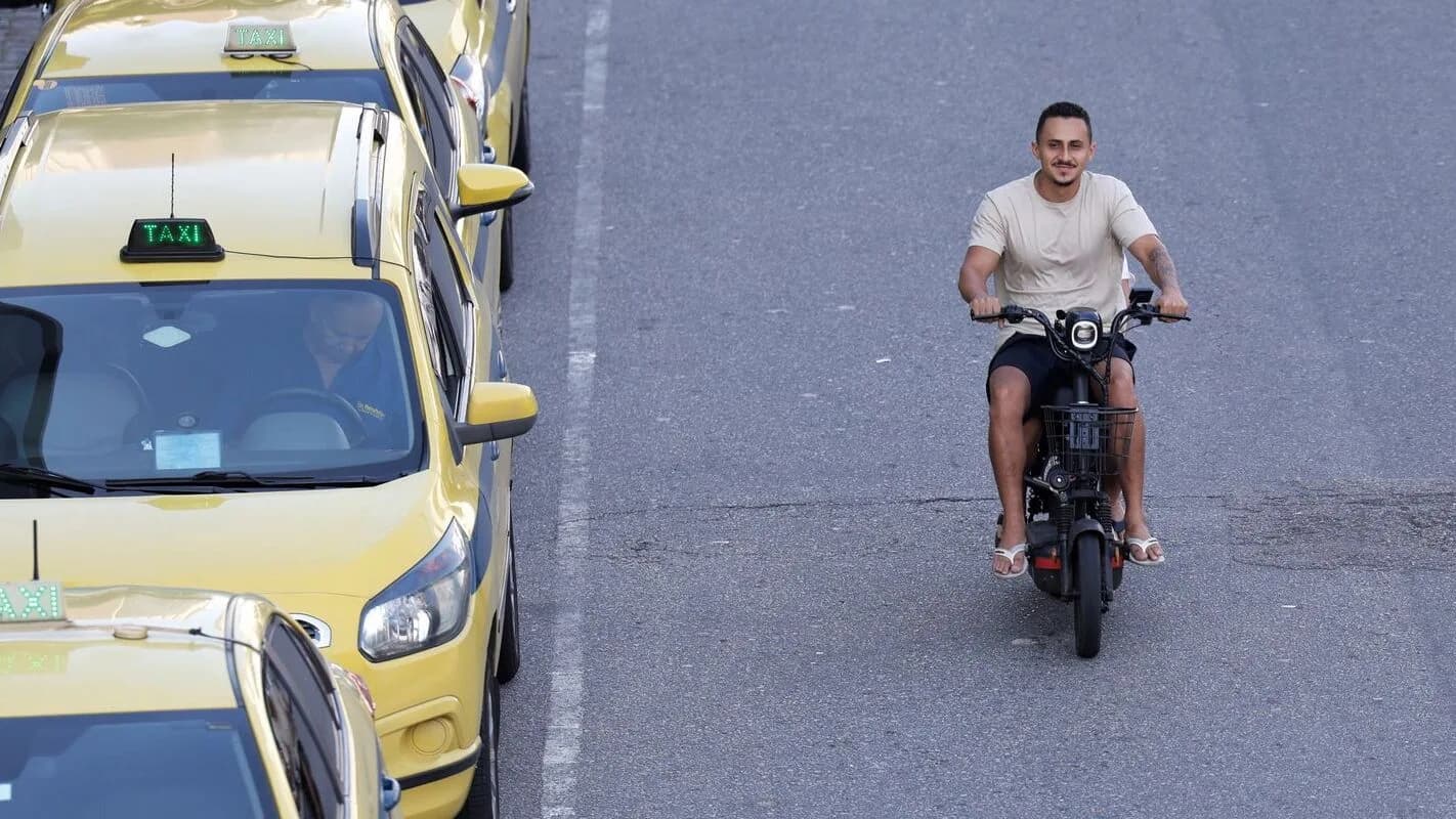 Motoboy conduz moto em via pública ao lado de táxis amarelos