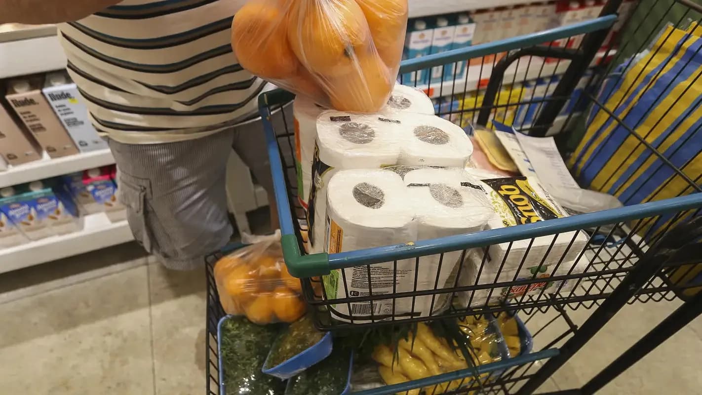 Consumidor coloca produtos em carrinho de supermercado, com prateleiras ao fundo