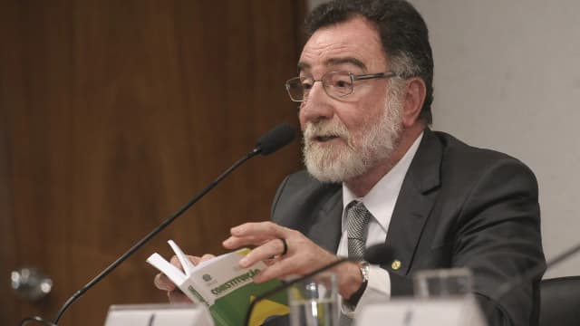 Patrus Ananias fala ao microfone segurando um exemplar da Constituição