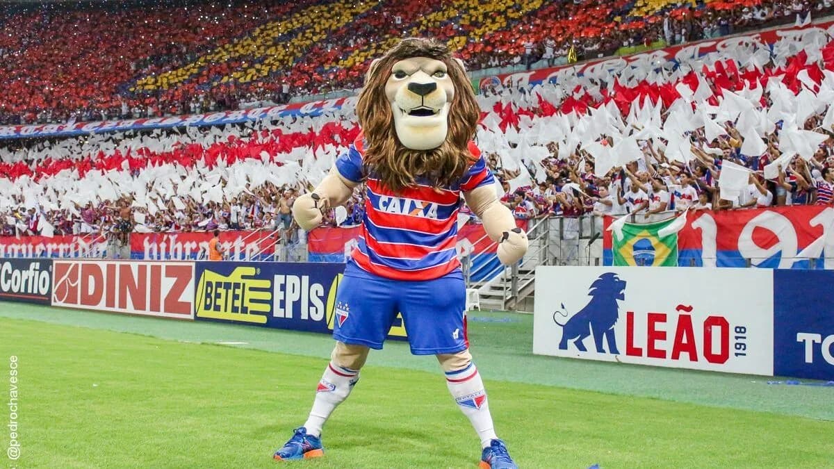 Mascote do Fortaleza, o leão Juba, em campo com a torcida tricolor ao fundo em jogo no Castelão