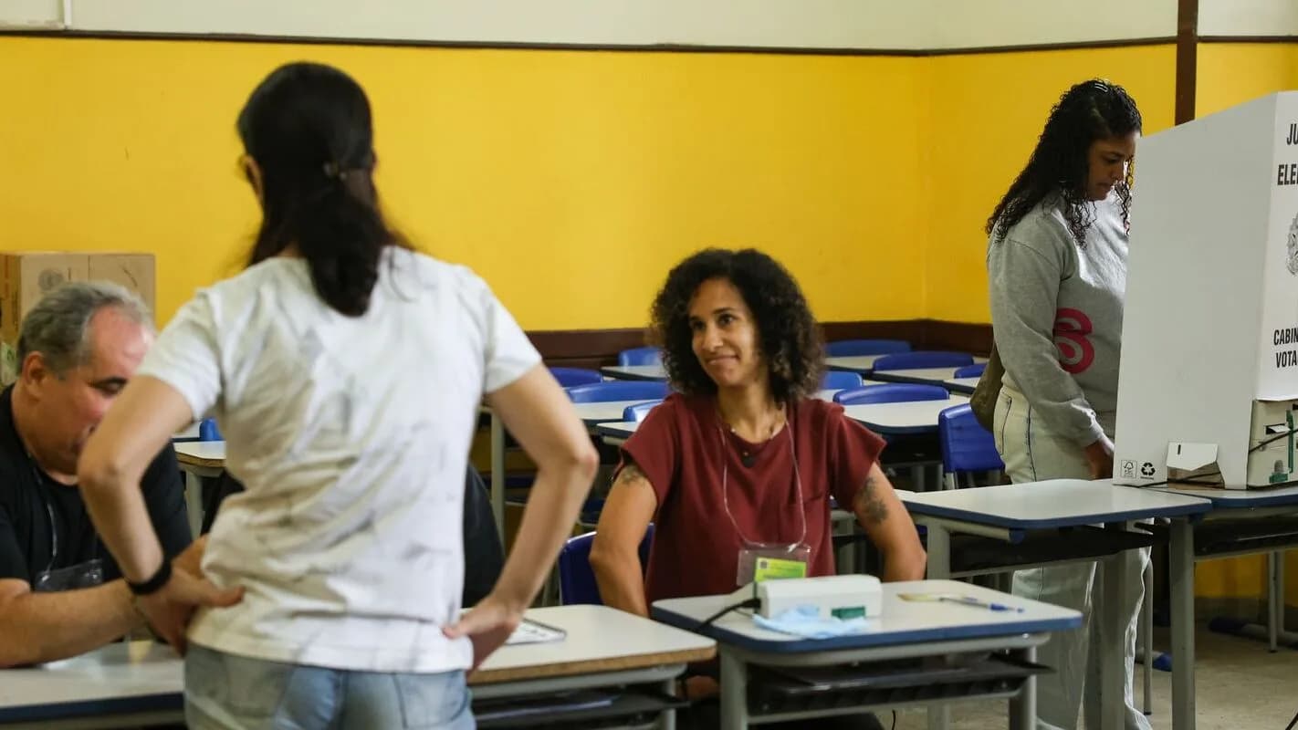 Eleitores em seção de votação com cabine eleitoral ao fundo