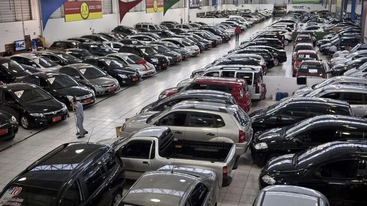 Vista aérea de um pátio de loja de veículos usados, com carros enfileirados e um funcionário caminhando entre eles