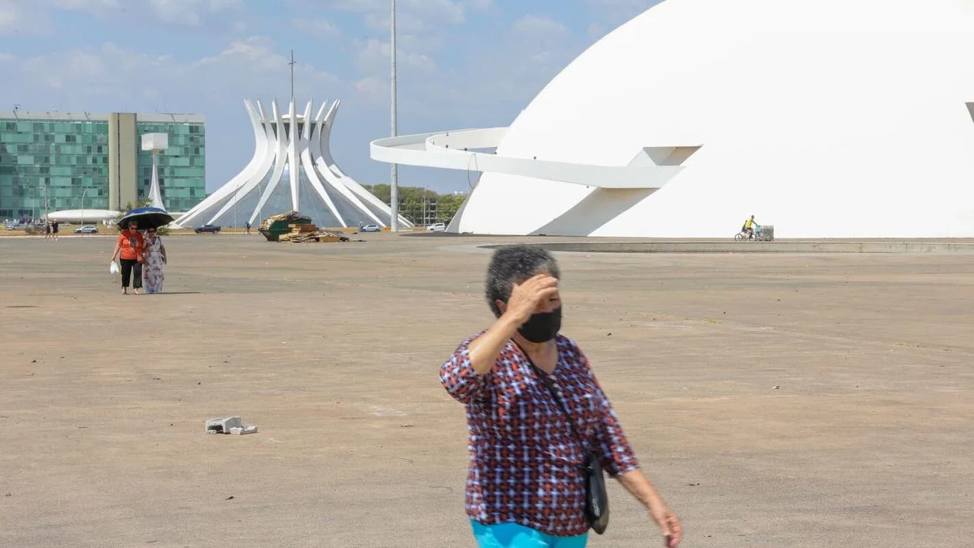 Pessoa se protege do calor com a mão sobre os olhos em Brasília, com o Congresso Nacional ao fundo