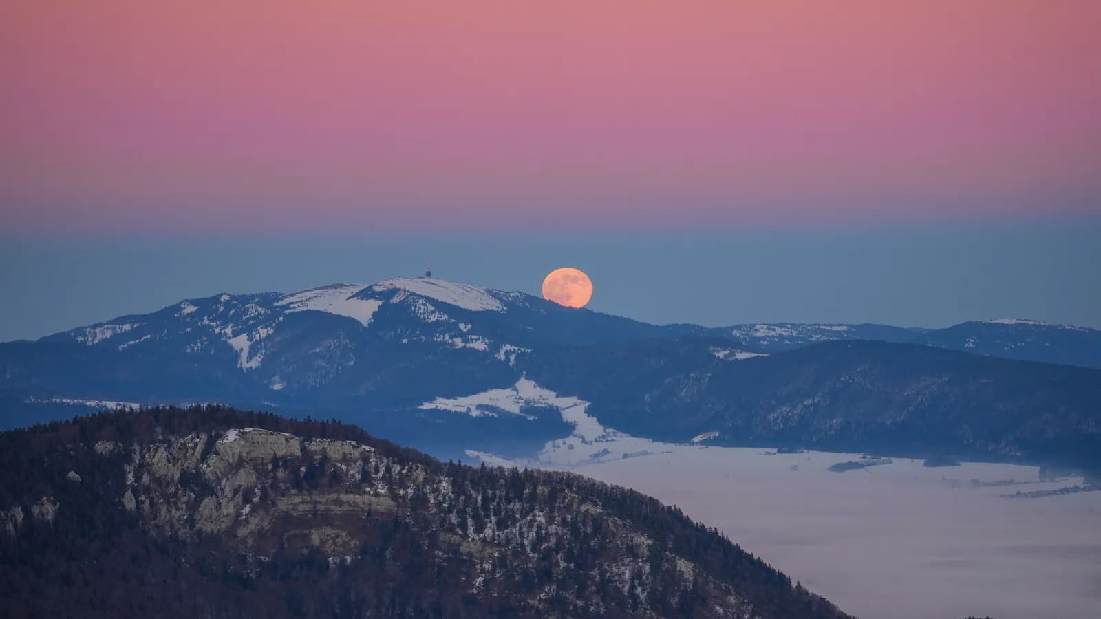 Lua cheia alaranjada surgindo no horizonte ao entardecer, atrás de uma montanha