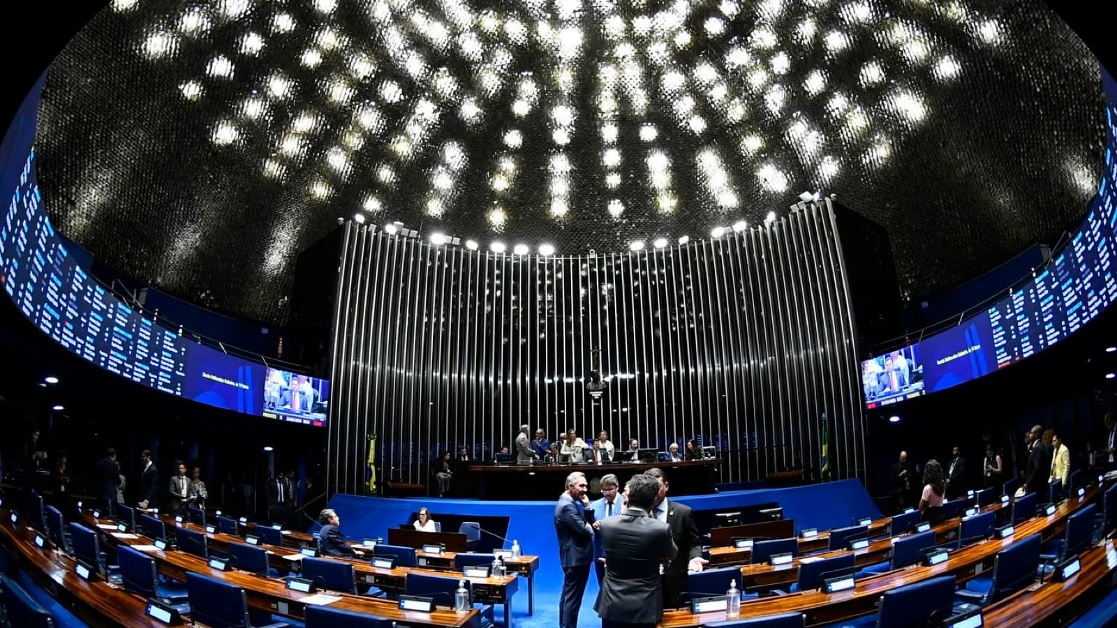 Plenário do Senado Federal durante sessão, com senadores em pé conversando e mesa diretora ao fundo