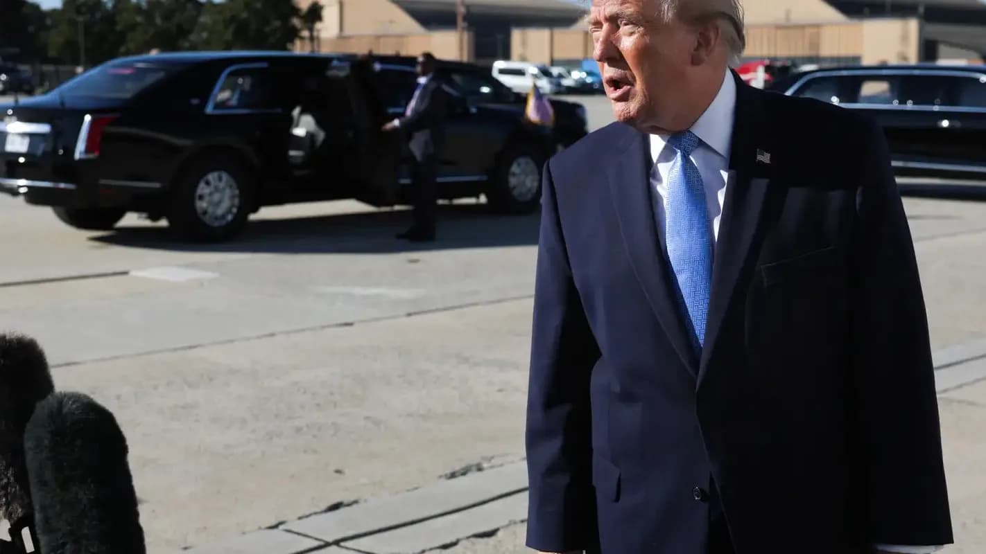 Donald Trump caminha ao lado de carros oficiais, cercado por microfones de jornalistas