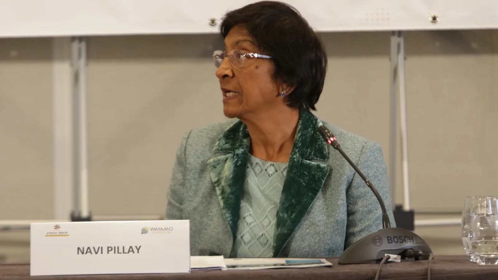 Navi Pillay fala ao microfone em painel com placa de identificação com seu nome
