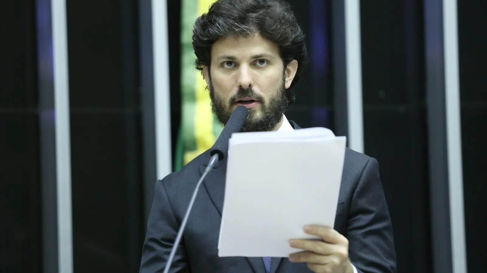 Marcelo Aro fala ao microfone em audiência pública, de terno escuro e barba