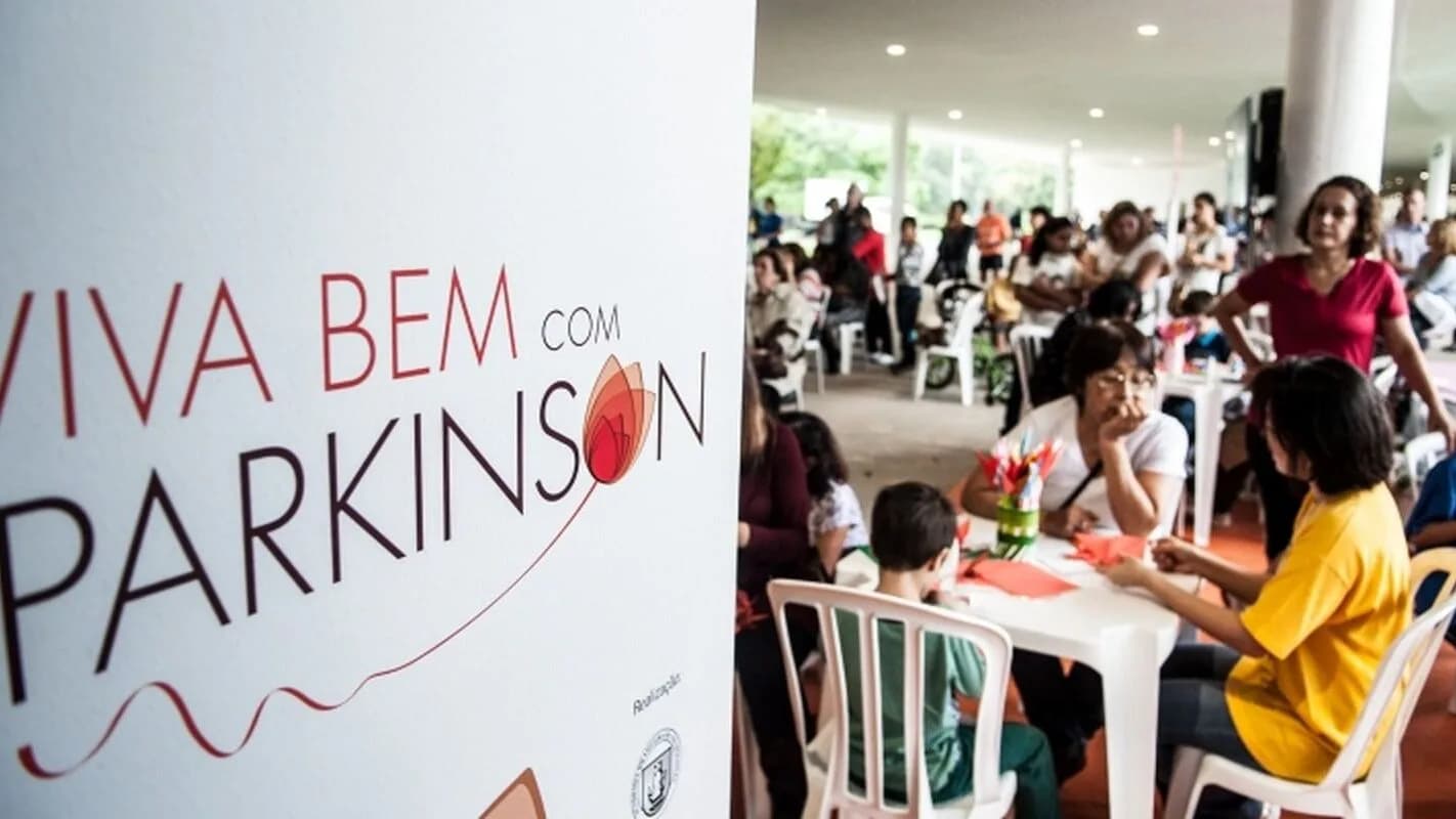 Banner da campanha Viva Bem com Parkinson ao lado de pessoas reunidas em evento de conscientização sobre a doença