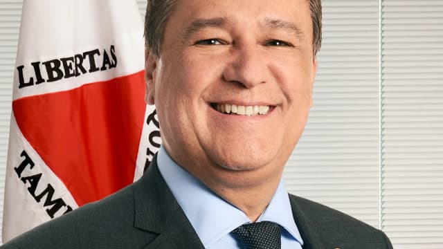 O senador Carlos Viana (PSD-MG) sorrindo, em retrato oficial, com a bandeira de Minas Gerais ao fundo