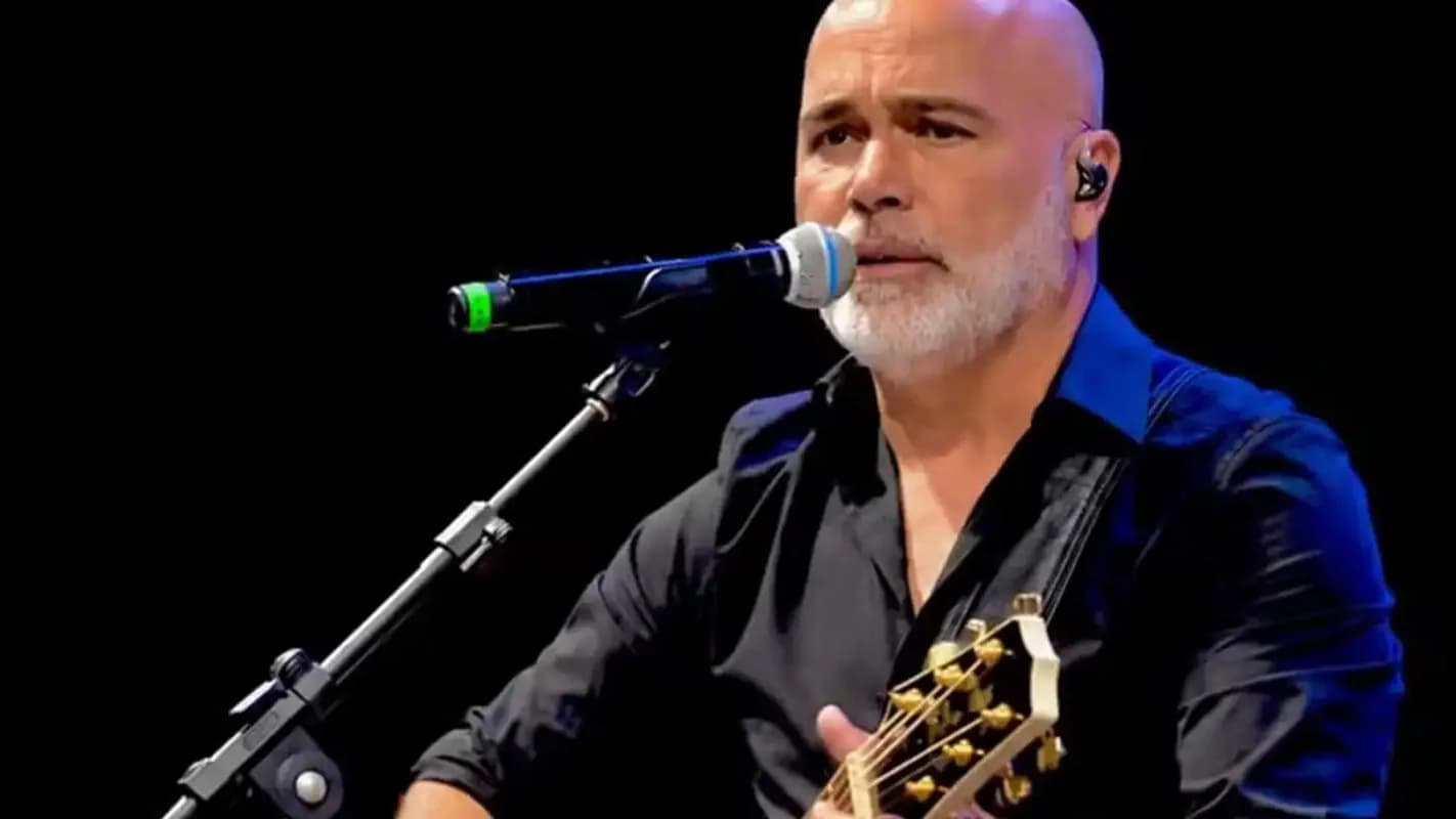 O cantor Rick canta ao violão em um show, com microfone à frente