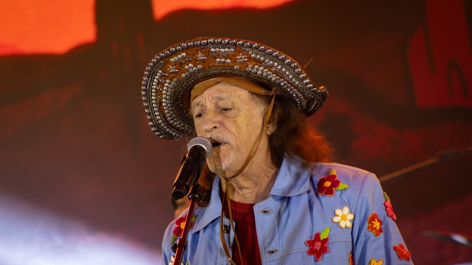 Alceu Valença canta ao microfone, de chapéu de couro decorado com estrelas e tachas e jaqueta jeans bordada com flores, em show de 2024 — imagem de arquivo