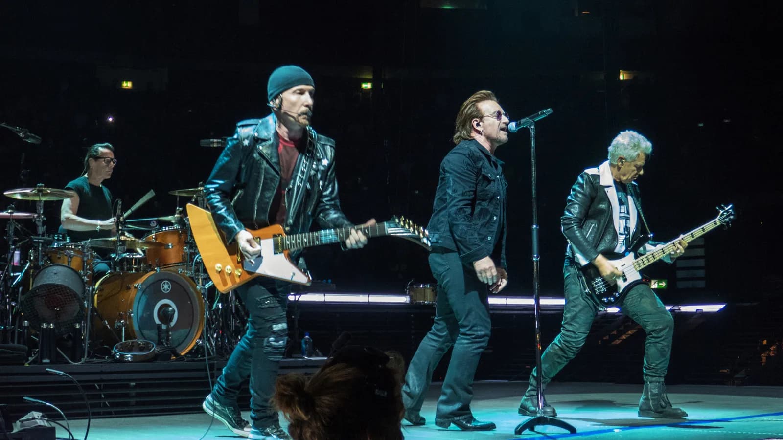Banda U2 se apresenta ao vivo no palco durante turnê, com Bono no vocal e os demais integrantes tocando