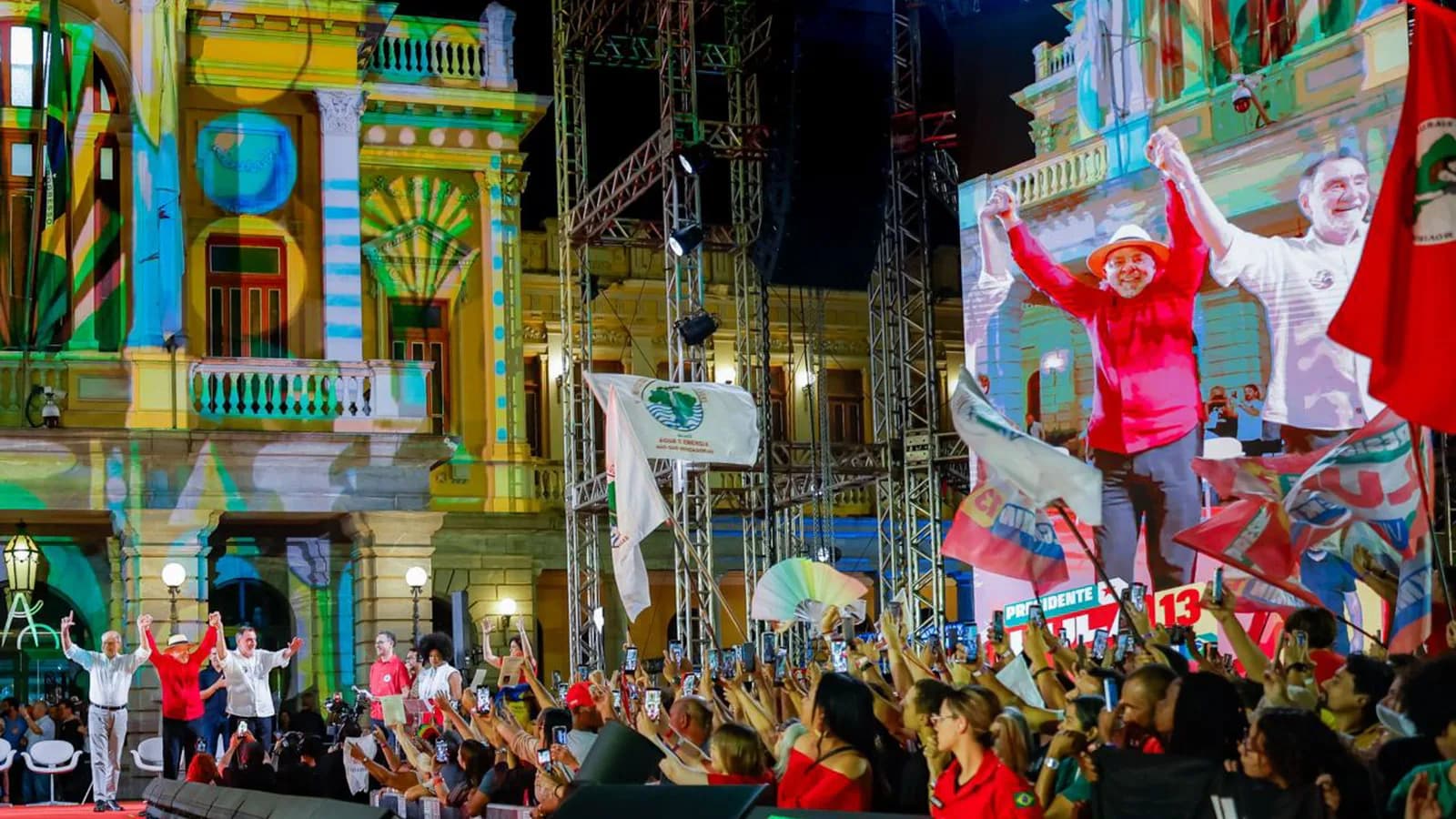 Público acompanha comício de campanha do PT em Belo Horizonte, com telão exibindo Lula e bandeiras vermelhas