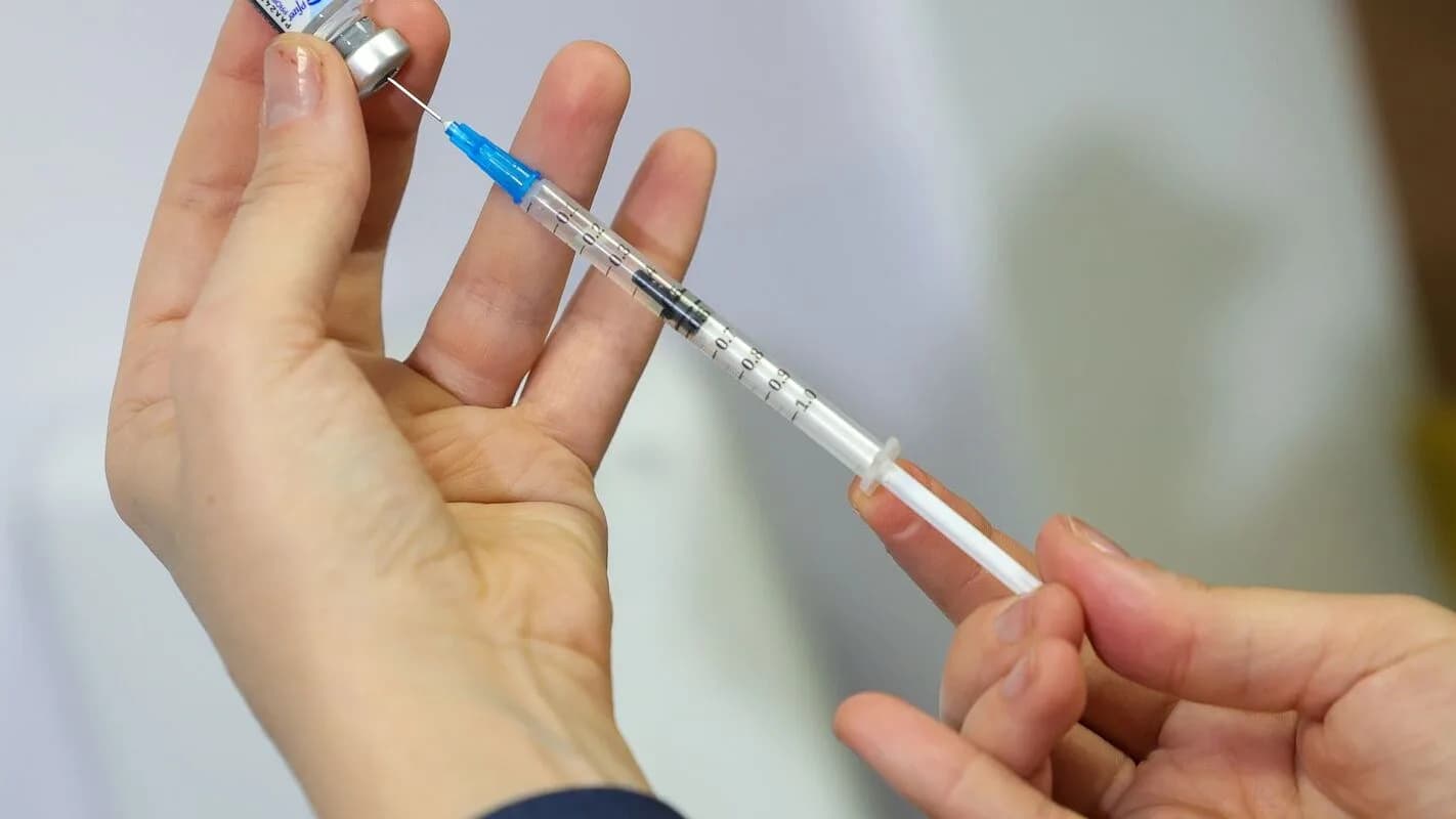 Mãos preparando uma seringa com dose de vacina para aplicação