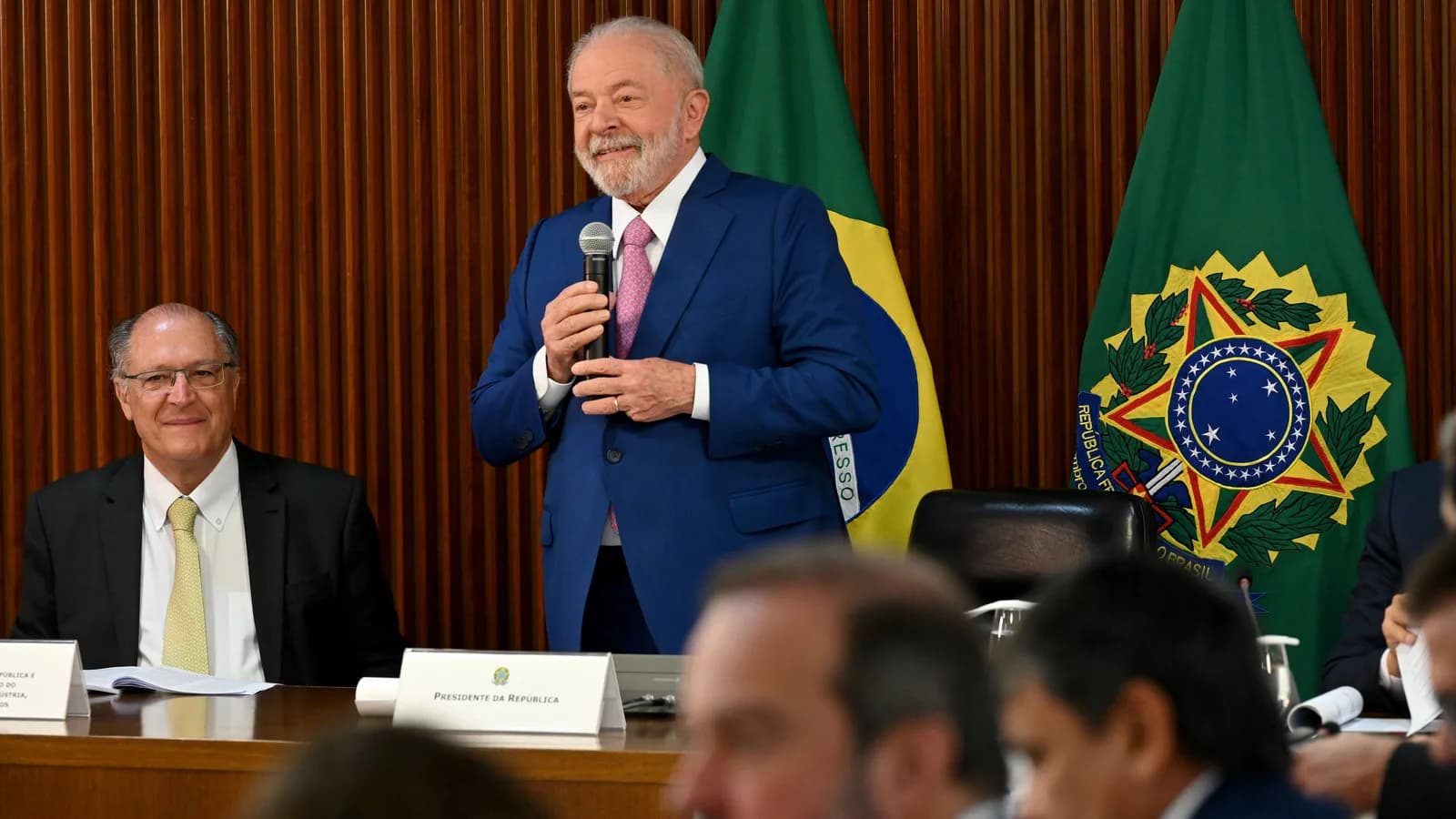Lula discursa de pé em reunião ministerial, ao lado de Geraldo Alckmin, com bandeiras ao fundo