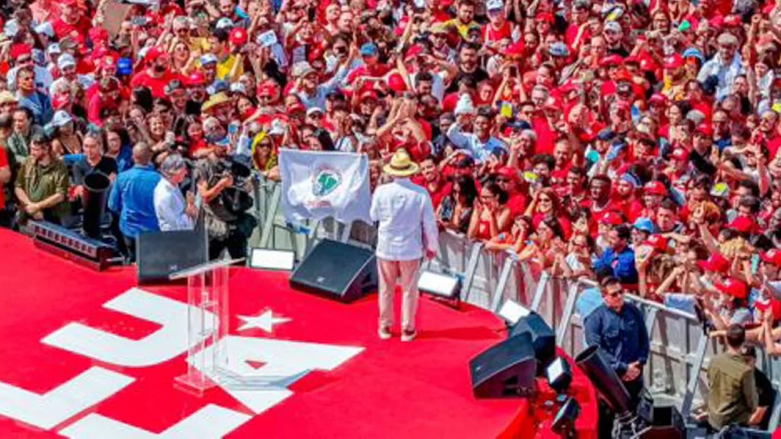 Lula, de camisa branca e chapéu, acena de costas para multidão de apoiadores durante o lançamento oficial de sua campanha presidencial
