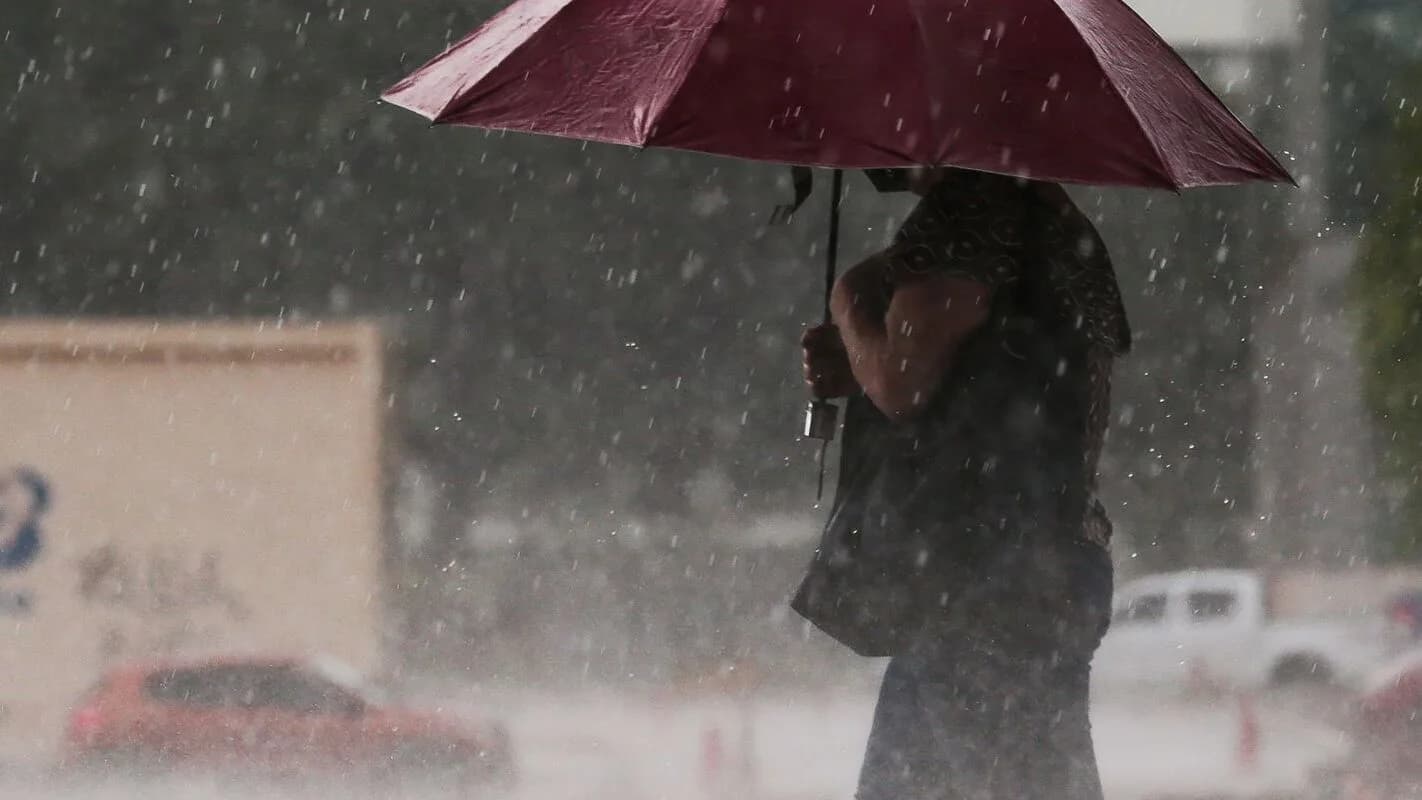 Pessoa com guarda-chuva vermelho protege-se de chuva forte em via urbana
