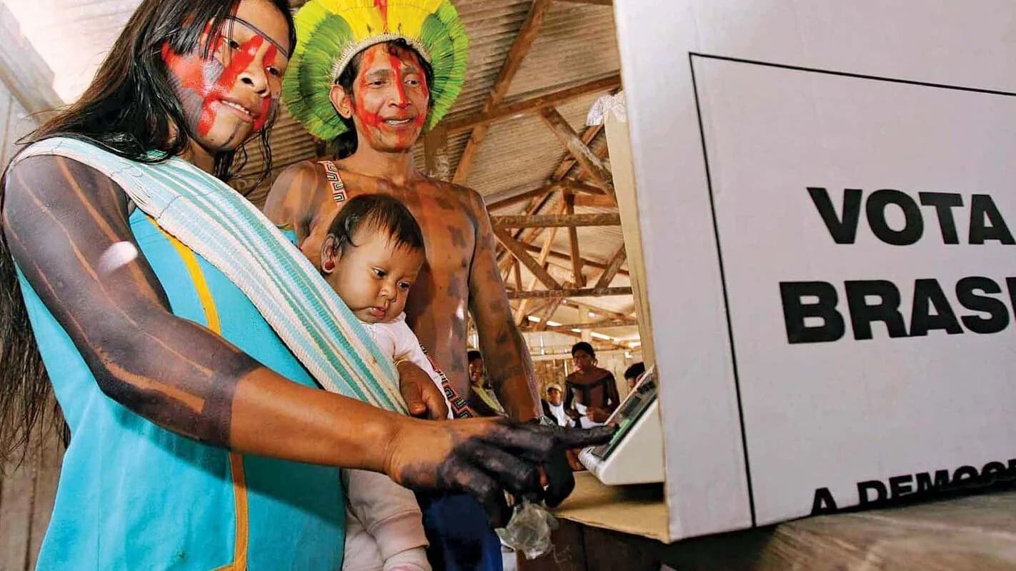 Indígena do Vale do Javari vota em urna eletrônica com cartaz 'Vota Brasil' ao fundo
