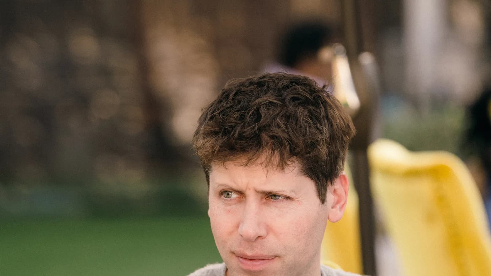 Sam Altman, CEO da OpenAI, com expressão pensativa, sentado ao ar livre