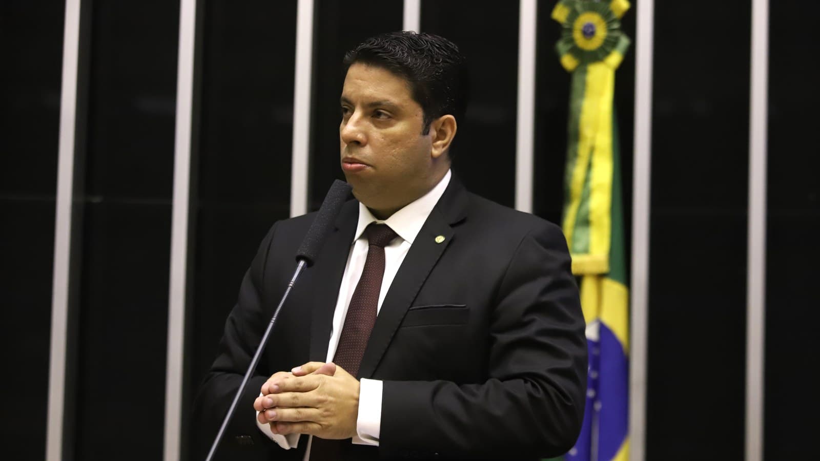 O deputado federal Igor Timo discursa na tribuna do plenário da Câmara dos Deputados, com microfone à frente e a bandeira do Brasil ao fundo, em imagem de arquivo de 2021