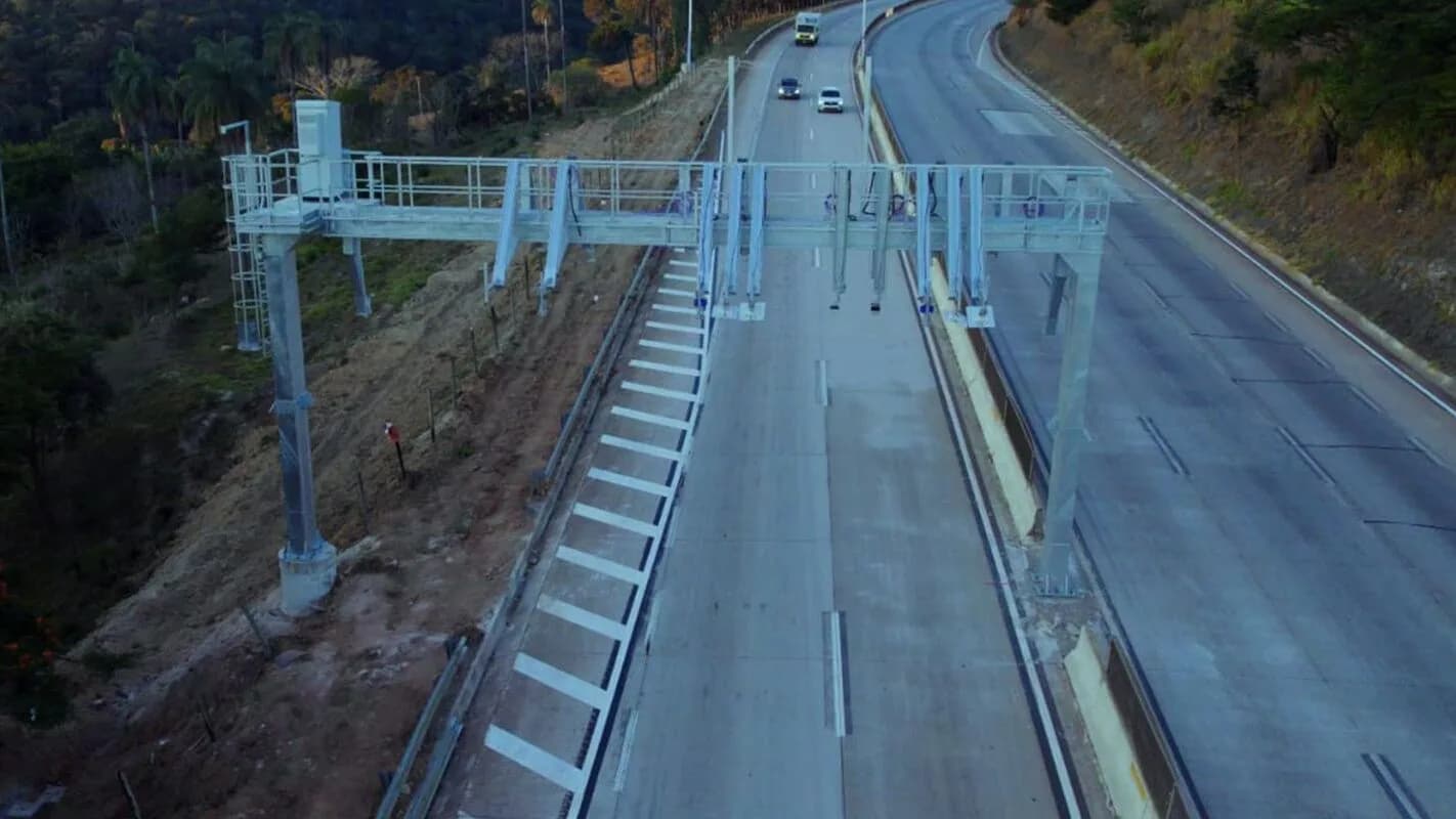Vista aérea de trecho da rodovia BR-381 com pórtico de pedágio eletrônico, sem veículos no momento do registro