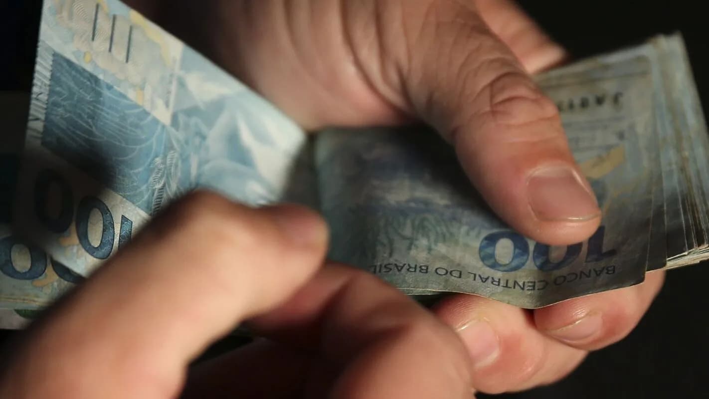 Mão conta cédulas de dinheiro do Banco Central do Brasil