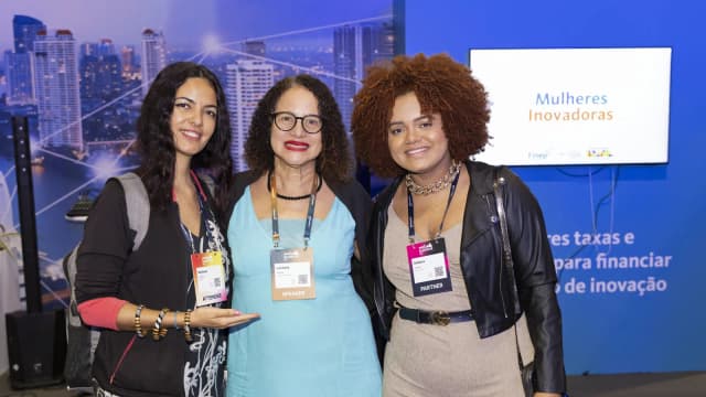 Luciana Santos entre duas mulheres em evento de inovação, com crachá de palestrante