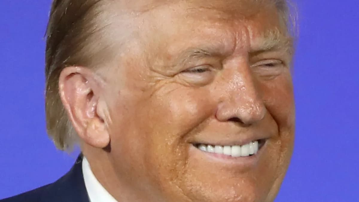 Donald Trump sorri durante evento público, vestindo terno escuro e gravata azul