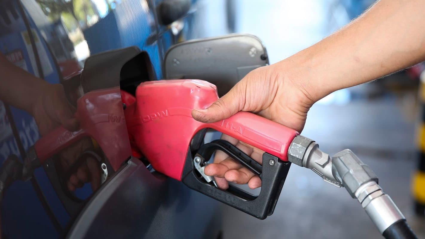 Mão de motorista segura bico de bomba abastecendo veículo com combustível em posto de gasolina
