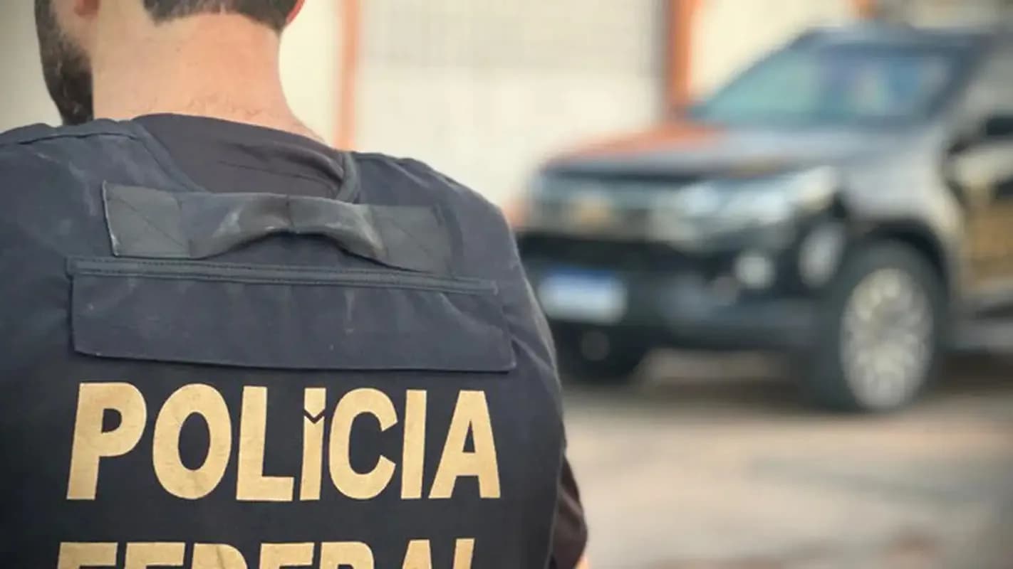 Agente da Polícia Federal de costas, com colete da corporação, em frente a uma viatura durante operação