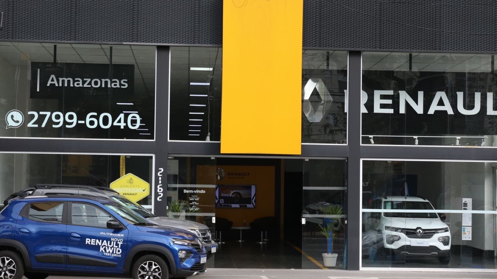 Imagem de arquivo: fachada de uma concessionária de veículos, com um carro azul estacionado na calçada e outro modelo branco exposto atrás do vidro da loja