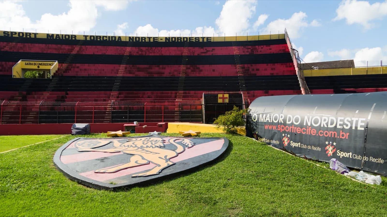 Estádio Ilha do Retiro, em Recife, com o brasão do Sport Club do Recife pintado no gramado e a arquibancada listrada em vermelho e preto ao fundo