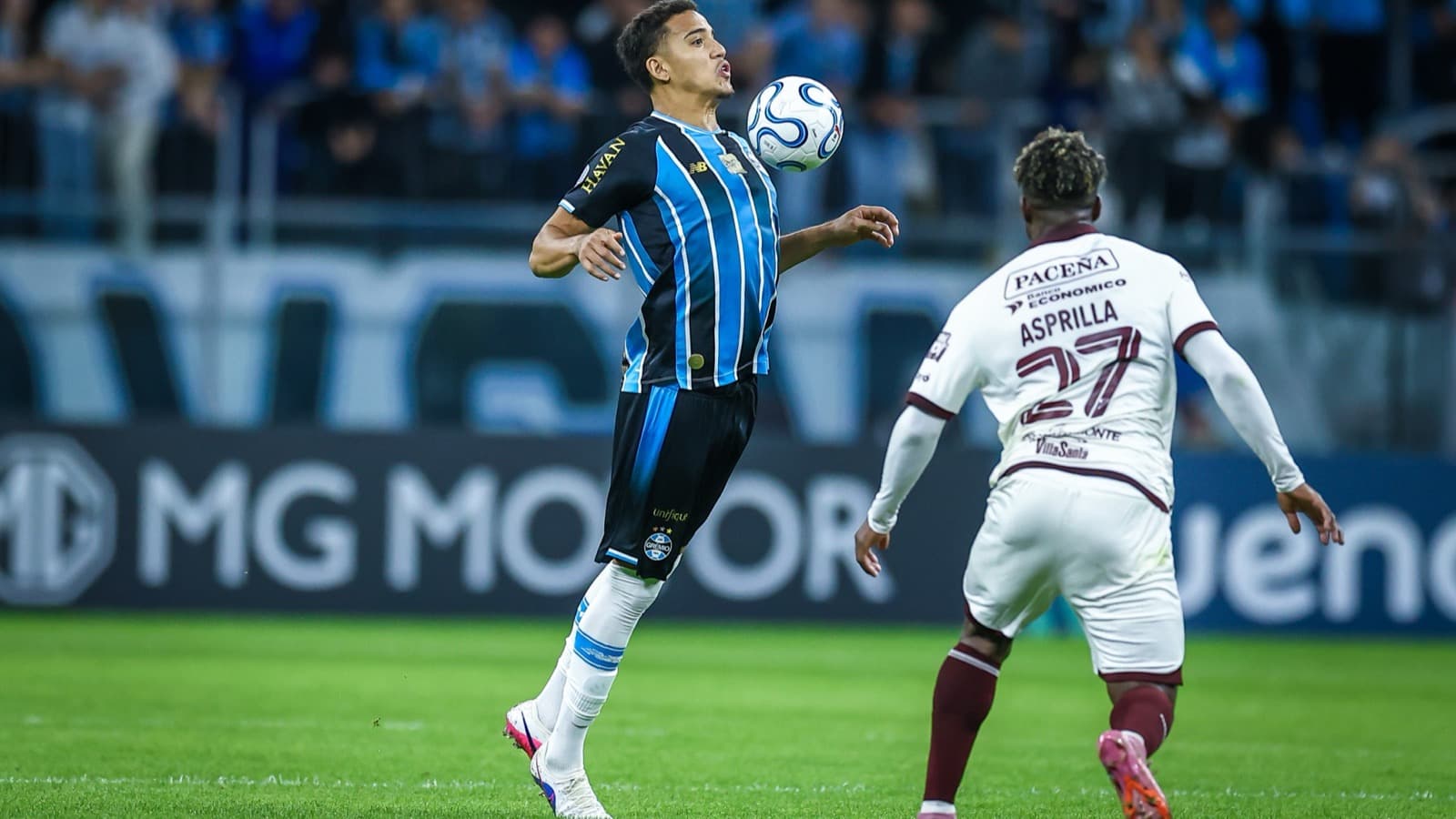 Jogador do Grêmio, de camisa tricolor, domina a bola no peito enquanto Asprilla, do Bolívar, se aproxima durante a partida na Arena