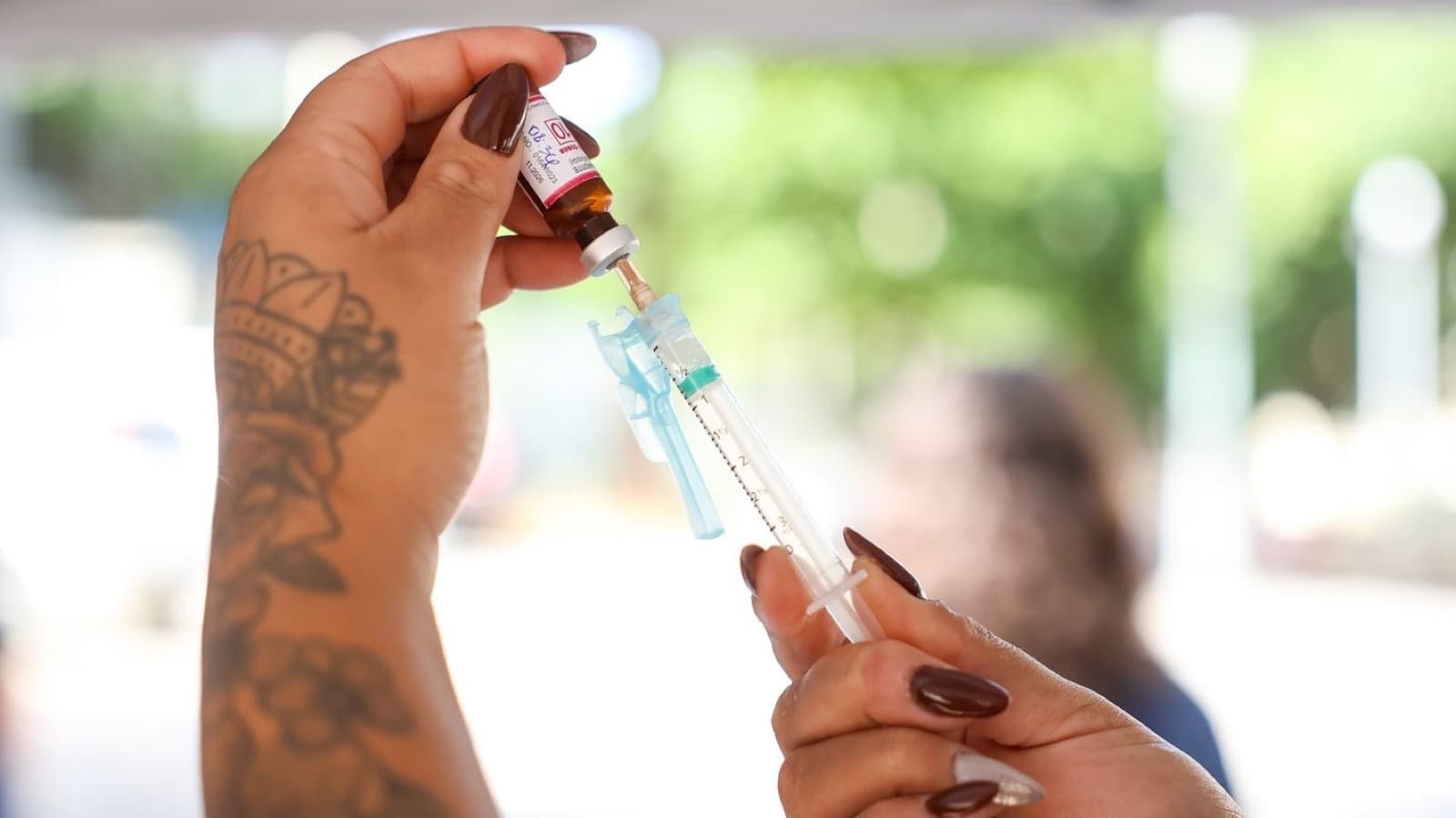 Imagem de arquivo das mãos de uma profissional de saúde aspirando uma dose de vacina de um frasco-ampola para dentro de uma seringa