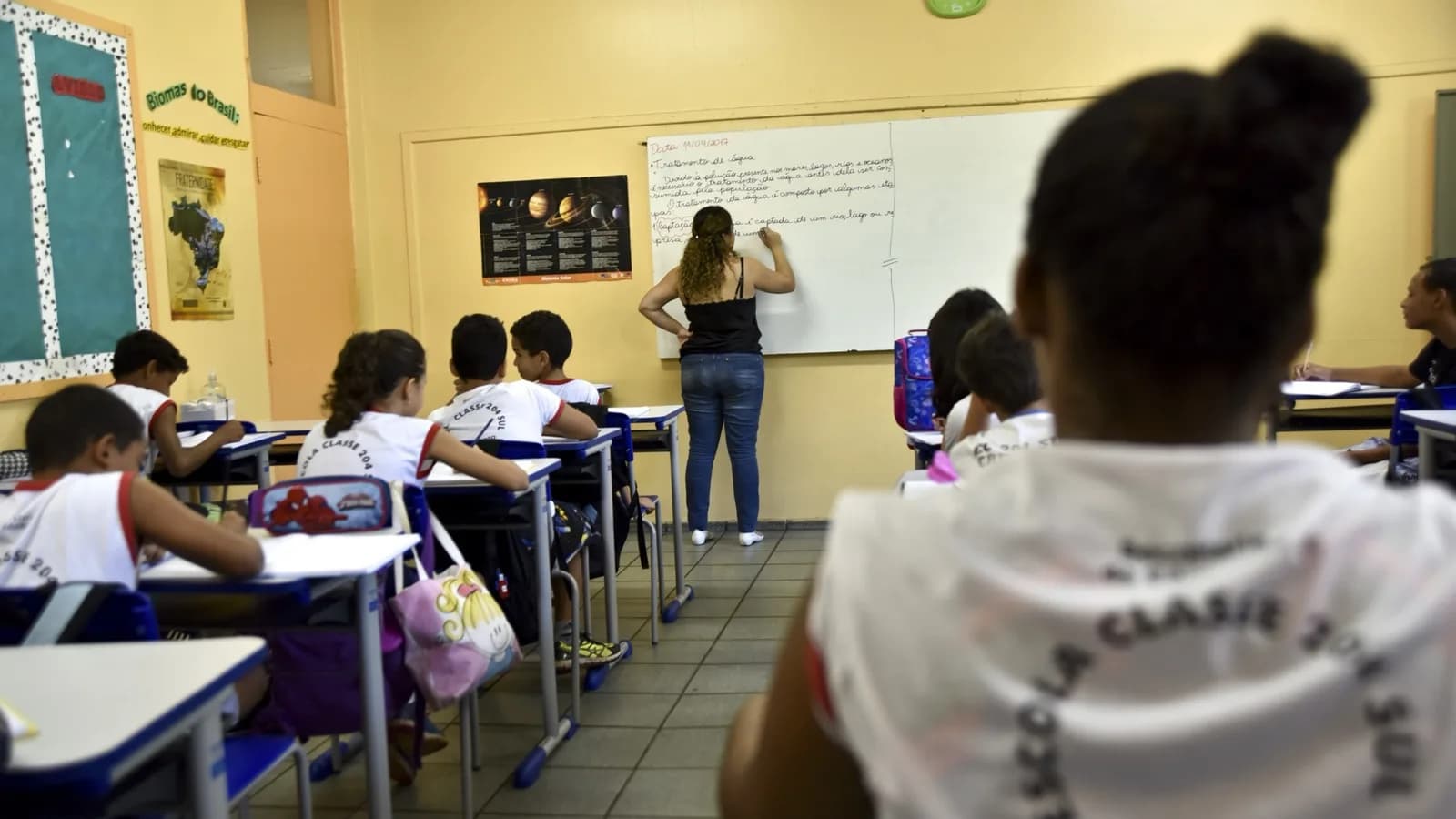 Professora em sala de aula de escola pública do Distrito Federal, com alunos nas carteiras